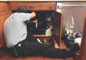 plumber working on a broken pipe under the sink